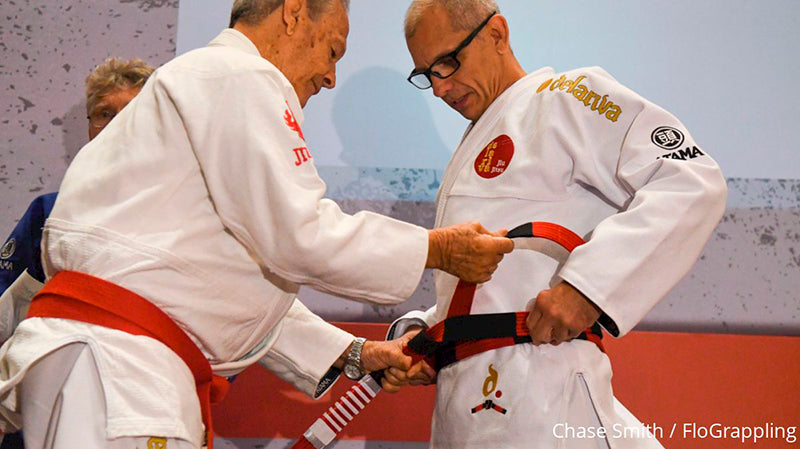 Ricardo De La Riva receiving his 7th degree red and black coral belt in a promotion ceremony, symbolizing his long career and contributions to Jiu Jitsu.