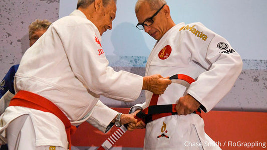 Ricardo De La Riva receiving his 7th degree red and black coral belt in a promotion ceremony, symbolizing his long career and contributions to Jiu Jitsu.